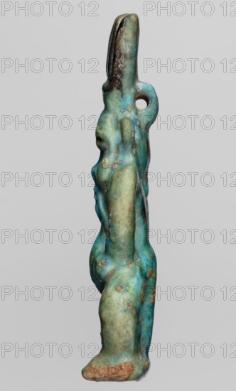 Amulet — god Bes; creator, subject: Bes Egyptian deity; period: 664–332 BC, Late Period, Egypt; type: amulet; dimensions: height 7.2 cm, width 3.2 cm., A vertical sculptural object photographed against a light gray background showing a side profile of a stylized figure with elongated head and rounded body forms; the surface displays a weathered, mottled appearance with a mix of turquoise, aqua, green, and patches of darker brown and black patina, as well as areas of lighter beige and sandy discoloration; the figure has a rounded protruding nose and breasts, a pronounced rounded posterior and legs, and a loop-like projection near the neck area; textures range from smooth to pitted with small rough spots and worn edges.