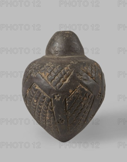 Spheroconic vessel, deposit provenance unspecified, Polish-French excavations in Edfu Egypt, Islamic art, Arabic culture, Mamluk Sultanate 1250–1517. Ceramics — Arabic/Egyptian ceramics; possibly a Mamluk bomb or aeolip. 13th–14th century, Egypt. Vessel, height 12.0 cm, diameter 8.7 cm. The surface of the belly is decorated with rhomboidal fields with a scale motif, also present on the collar, and rosettes in the stripes separating the fields of decoration. Salt glazing ., A dark brown, rounded ceramic vessel with a narrow, slightly domed neck and bulbous body sits against a light gray background; the vessel's surface shows carved, repeating scale-like patterns arranged in panels and separated by raised, angular ridges, with small floral or rosette motifs interspersed, and areas of lighter brown wear where the carved details catch the light.