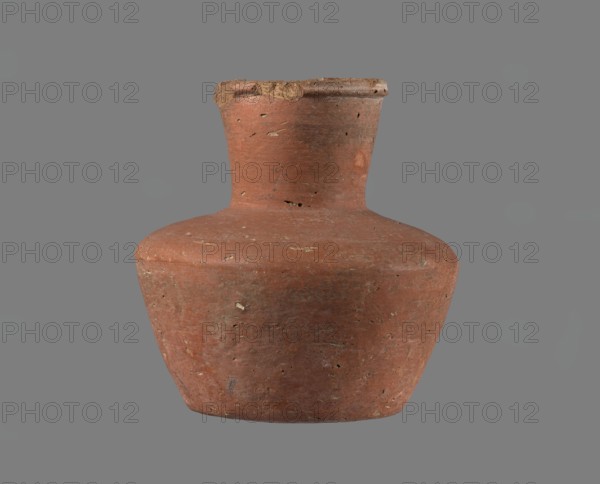Jug, Small jug without a handle with a biconical body, widest at about half its height. Broad, rather flat shoulders. Wide, almost cylindrical neck widening slightly toward a profiled, irregular spout that slopes down on one side and extends to form a small pouring lip; spout cross-section triangular with an approx. 1 mm indentation at the centre of the outer profile. Neck shaped separately and attached to the shoulders. Bottom almost flat, very slightly rounded. Made of Nile clay NB1/2 Vienna System. Outer surface and inner surface of rim and neck leveled and covered with an engobe and polished/smoothed; remaining inner surface leveled. Color red-brown. Almost complete small fragment of rim missing; outer surface slightly worn in places. Origin: Edfu Old Kingdom; attributed to 4th–6th Dynasty; c. 2686–c. 2181 BC. Vessel; height 11.4 cm; rim diameter 5.5 cm; shoulder diameter 10.8 cm; bottom diameter 7.1 cm., A single earthenware vessel with a wide rounded body and a narrow neck topped...