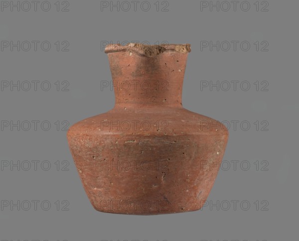 Jug, A small clay jug without a handle with a biconical body, widest at about half its height. Broad, rather flat shoulders; a separately shaped neck glued to the shoulders, wide and almost cylindrical, about one-third of the vessel's height and widening slightly toward the profiled spout. The spout is irregular, sloping down on one side and extending to form a small pointed lip; in cross-section it is roughly triangular with an approximately 1 mm central indentation on the outer profile. Bottom almost flat, very slightly rounded. Made of Nile clay NB1/2? per Vienna System. Outer surface and inner rim/neck are smoothed and covered with an engobe; remaining inner surface smoothed. Color red-brown. Nearly complete with a small fragment of the rim missing; outer surface slightly worn in places. Probably Old Kingdom 4th–6th Dynasty, c. 2686–2181 BC. Vessel; height 11.4 cm; rim dia. 5.5 cm; shoulder dia. 10.8 cm; bottom dia. 7.1 cm., A weathered clay vessel with a rounded body and a narrow ...