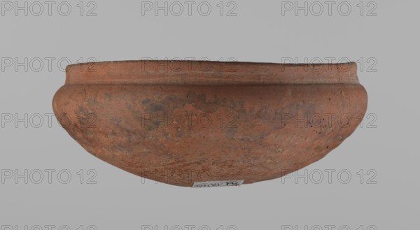 Medum-type bowl, Ceramics: Egyptian pottery vessel, clay bowl with hemispherical shape. The walls bend gently around about 2/3 of the height; rim straight and perpendicular to the shoulders, slightly irregular; rounded bottom. Surface even; vessel color red. Assembled from several fragments. c. 2686–c. 2181 BC Old Kingdom, from Edfu. Vessel; height 5.5 cm, diameter 12.6 cm rim, diameter 13.5 cm shoulders., A broad, shallow clay vessel with a rounded body and a slightly flared rim sits against a plain light gray background, showing a rough, weathered surface with mottled reddish-brown and darker brown areas and some small pits and specks of lighter beige.