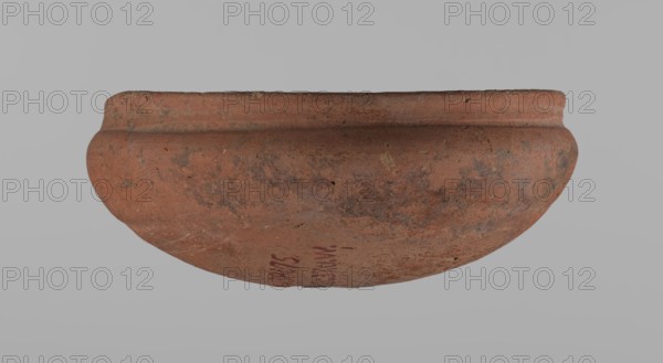 Medum-type bowl, ceramics; Egyptian pottery vessel, clay bowl with hemispherical shape. The walls bend gently around about 2/3 of the height of the vessel. The rim is straight, perpendicular to the shoulders, slightly irregular. Rounded bottom. The surface of the vessel is even. Vessel colour: red. Vessel glued together from several fragments. c. 2686–c. 2181 BC; Old Kingdom, Edfu place of origin. Vessel, height 5.5 cm; diameter 12.6 cm rim, 13.5 cm shoulders., A round, shallow clay bowl shown from the side with a rounded body and a slightly raised rim, displaying an overall reddish-brown color with patches of darker brown and gray weathering; the surface has a few small pits and rough spots and the background is a uniform light gray.
