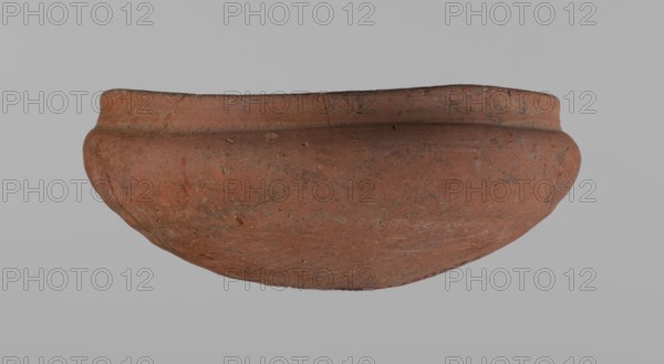Medum-type bowl, Ceramics; Egyptian pottery; clay vessel. Bowl with a hemispherical shape: walls bend gently around about 2/3 of the height, straight rim perpendicular to the shoulders slightly irregular, rounded bottom. Surface even; vessel color red. Vessel glued together from several fragments. c. 2686–c. 2181 BC Old Kingdom, from Edfu. Vessel; height 5.5 cm, rim diameter 12.6 cm, shoulder diameter 13.5 cm., A large rounded clay bowl with a worn rim sits against a plain light gray background, showing an overall reddish-brown surface with patches of darker brown and small grayish specks, rough texture, visible scuffs and small pitted marks, and a subtle raised band near the rim.