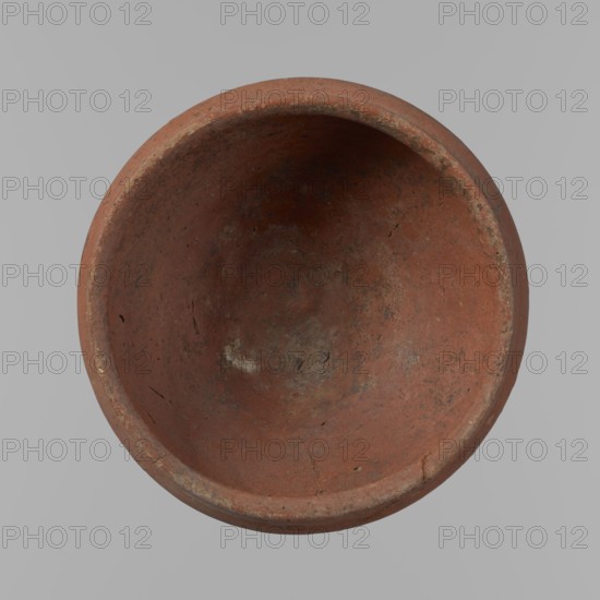 Medum-type bowl, ceramics; Egyptian pottery vessel clay, Medum-type bowl with hemispherical shape. Walls bend gently around about 2/3 of the vessel height. Straight rim, perpendicular to the shoulders, slightly irregular. Rounded bottom. Even surface. Red color. Reconstructed from several glued fragments. c. 2686–c. 2181 BC Old Kingdom, from Edfu. Vessel; height 5.5 cm; diameter 12.6 cm rim, 13.5 cm shoulders., A round, shallow bowl viewed from above with a worn, coarse surface in shades of reddish-brown and terracotta, showing patches of darker brown and grayish discoloration and a few lighter, pale spots; the rim is slightly raised and shows scuffs and rough edges in muted tan and off-white tones, and the interior has small scratches and irregular marks with subtle variations of red, brown, and gray throughout, set against a plain light gray background.