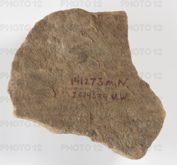 The Hor Hieroglyph - relief fragment, Horus mythology. Relief fragment with several preserved hieroglyphic signs. The preserved fragment features a schematic representation of a falcon the Hor sign shown in right profile, above which three ball-like signs and a triangular sign are preserved. Sections of the side frames remain. 3rd–1st century BC, Ptolemaic Period, Edfu. Inscription, bas-relief; height 17 cm, width 16 cm, depth 3 cm., A roughly triangular piece of coarse textured stone with an uneven, jagged edge, displaying a sandy brown surface with areas of darker brown and hints of gray; there is a patch of reddish pigment visible near the center of the stone.
