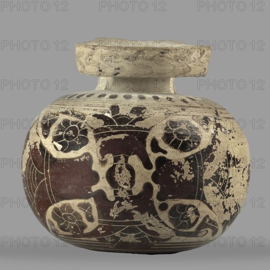 Orientalizing aryballos with depictions of lotus flowers;, repossession Silesia; lotus iconography; vessel for oils and ointments; Greek pottery; 580–570 BC; Corinth; vessel aryballos; height 6.8 cm; width 7.4 cm; weight 0.112 kg., A rounded ceramic jar with a short neck and a flat, wide rim sits against a plain gray background; the jar shows a worn painted surface with a cream base color and large areas of dark brown and black decoration forming curved, floral and abstract shapes, and there are patches of lighter beige where the finish has chipped, giving an aged, distressed appearance.