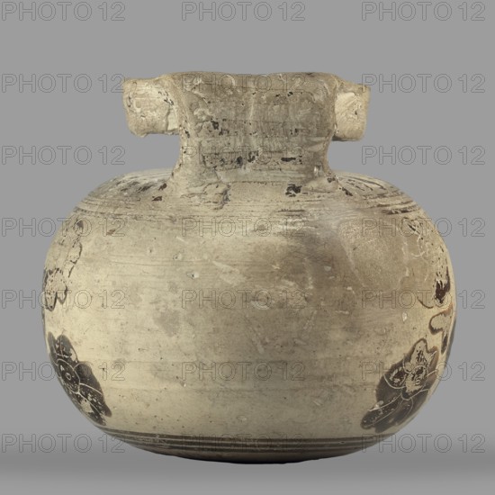 Orientalizing aryballos with depictions of lotus flowers, lotus motifs, vessels for oils and ointments, Greek pottery, 580–570 BC, Corinth, vessel aryballos, height 6.8 cm, width 7.4 cm, weight 0.112 kg, A rounded ceramic vessel with a short, wide neck and a thick, horizontal handle sits against a plain gray background. The vessel surface is predominantly beige and light tan with areas of darker brown discoloration and worn patches. There are several dark brown floral-like motifs and smudges decorating the lower sides, and faint horizontal incised lines encircle the body near the base and neck. The handle and neck show rough texture and chipped areas with darker flecks, and the overall finish appears weathered and aged.