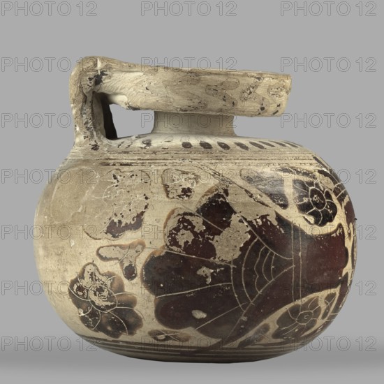 Orientalizing aryballos with depictions of lotus flowers; maker, used for oils and ointments; Greek pottery, Corinth; dated 580–570 BC; pottery vessel aryballos; height 6.8 cm, width 7.4 cm, weight 0.112 kg., A rounded ceramic vessel with a short neck and a thick flat handle across the top, showing worn painted decoration. The surface colors include beige and off-white as the base, with dark brown and deep reddish-brown painted floral and abstract motifs, and small areas of blackened wear. The handle and upper rim show lighter beige with darker scuff marks, and the body displays several stylized flower shapes and large petal-like forms in dark brown against the lighter background. The vessel has areas of surface abrasion and chips revealing lighter clay beneath, and the image background is a uniform pale gray.