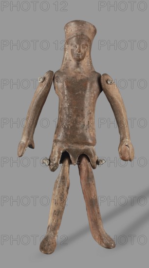 Doll with movable limbs, unknown Corinthian workshop, restitution provenance, toys, dolls, human figurines, 500–450 BC, Corinth place of origin?, figurine; height 13.9 cm, width 4.1 cm, depth 1.9 cm, weight 0.05 kg, A weathered humanoid figure made of brownish material with worn, earthy tones of tan and darker brown stands against a plain gray background, showing a rounded head with a simple facial depiction and a cap-like top, a torso that tapers to a skirt-like lower edge with scalloped openings, a pair of long, slightly curved arms attached at the shoulders with visible knotted cords, and two elongated legs that extend from the skirt area with rounded feet; the surface displays patches of lighter and darker brown, mottled discoloration, and signs of age or wear.