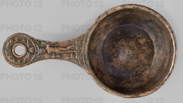 A ladle with a handle decorated with a depiction of Mercury, Mercury myth., Roman deities, ladles, 1st century, Roman Empire 27 BC–476, vessel; height 6.5 cm, width 25 cm, depth 13.5 cm, weight 0.62 kg, A shallow round metal bowl with an attached handle that ends in a circular loop, both showing a mottled surface of bronze, brown, dark brown, and greenish patina; the inner bowl surface has darker brown and black speckling and a ring of deeper discoloration toward the center; the handle displays low-relief decorative elements including curved motifs and a stylized human-like figure in low relief, all sharing the same aged bronze and brown tones with hints of green and darker spots on a pale gray background.