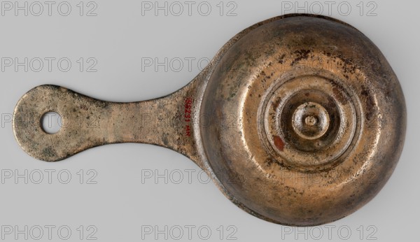 A ladle with a handle decorated with a depiction of Mercury, Mercury myth., Roman deities, ladles, 1st century, Roman Empire 27 BC–476, vessel; height 6.5 cm, width 25 cm, depth 13.5 cm, weight 0.62 kg, A metallic object with a rounded bowl-like end and an elongated handle, both showing a worn, pitted surface and areas of rough texture; the metal appears primarily bronze and brown with patches of darker brown and greenish corrosion and a few small reddish spots; the handle has a circular hole near its outer end and shares the same aged, speckled surface; the bowl end features concentric raised rings around a central raised knob, all showing similar wear and color variations against a neutral light gray background.