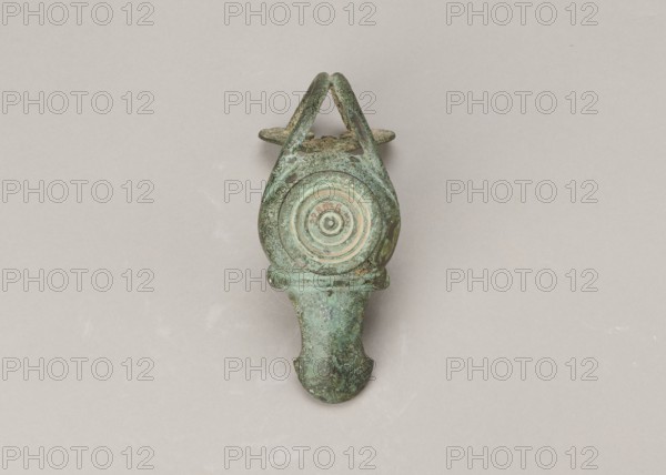 Oil lamp, 1st century, Pozzuoli, oil lamp, weight 0.524 kg; maker, Madeyski, Antoni 1862–1939 mentioned., An aged metal object with a greenish patina and areas of brown corrosion sits centered on a light beige background; it has a rounded top with a triangular loop extending upward, a circular recessed area with concentric rings near the upper middle, and a tapered lower section that flares slightly at the end, showing mottled textures and variations of green, turquoise, brown, and hints of darker grey.