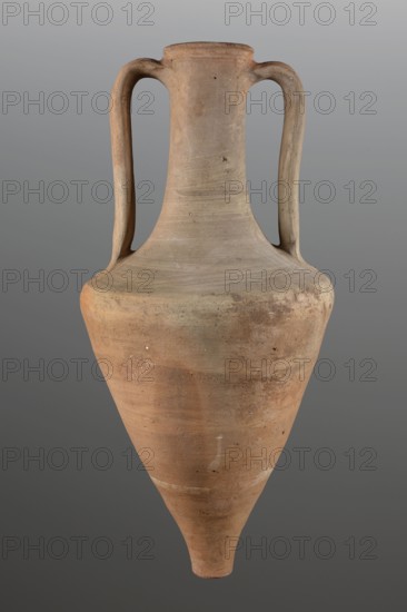 Transport amphora, trade amphora, 3rd quarter of the 4th century BC, Mende Greece. Vessel transport amphora made of ancient Greek ceramic; height 71 cm, diameter 33.5 cm. The walls of the body separate gently up to 2/3 of the height, then round markedly toward a long neck. The rim is defined by a profile and rounded into a cylindrical form. Flattened roller handles attached at the height of the rim fall vertically toward the narrowing of the body. Fingerprints present where the handles are attached on the body., An elongated, narrow-necked clay vessel with a pointed base and a flaring lip, shown upright against a neutral background; it has a pair of curved vertical handles attached near the rim and shoulder, a smooth rounded shoulder that tapers to a conical lower body, and a slightly flared mouth. The surface shows earthy tones of brown, tan, and muted orange with areas of lighter beige and subtle darker spots and smudges, along with a few small rough patches and speckles in similar n...