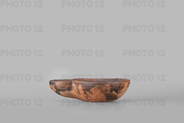 Lamp decorated with a depiction of a dog, unknown eastern workshop; single-burner oil lamp, 1st century, Roman Empire 27 BC–476; dogs iconography; weight 0.082 kg., A low, rounded object with an irregular, boat-like shape sits on a flat surface; its surface shows a mottled pattern of brown, dark brown, and black tones with patches of lighter brown and small speckled areas, and the top has a shallow recessed area while the sides curve smoothly and show wear and texture.