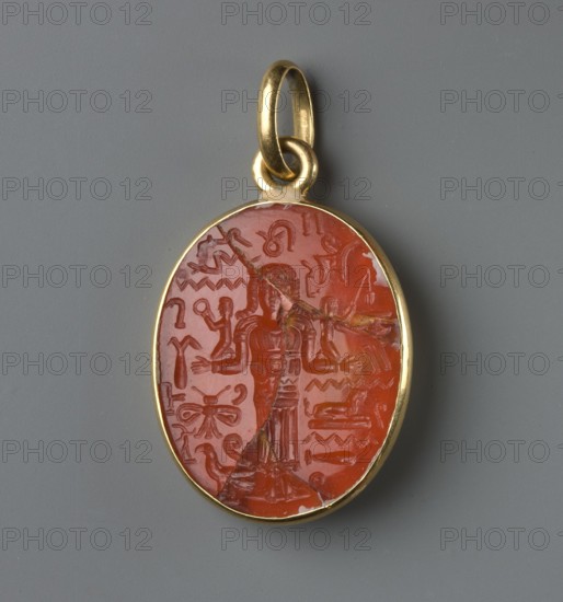 Medallion with a forged gem, France? Italy?, forgery of an oval gem set in a gold frame with an oval pendant. The gem's surface bears a carved image of a standing woman in a long robe with her arms bent at right angles in a gesture of prayer?. She wears a wig with curls falling over her shoulders. Various pseudo-hieroglyphs are carved around the figure. 17th–18th century; modern period, jewelry, weight 6.42 g, An oval pendant with a golden metal frame and loop, containing a polished reddish-orange stone carved with a central standing human figure and a surrounding array of abstract and decorative carved motifs; the stone shows a few visible cracks and fissures, and the background behind the pendant is a uniform medium gray.