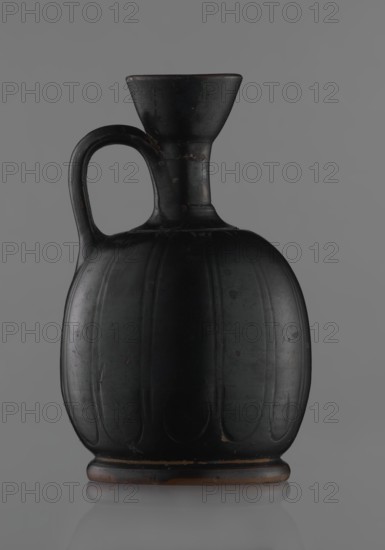 Black-finished aryballoi lekythos, Greek black-glazed pottery. Aryballoi lekythos coated with black varnish. Flat foot flows directly into a bulging body, significantly widened in its lower section. Nearly horizontal handles flow into a slender neck ending in a significantly widening, cup-shaped rim. Handle attached at the transition from body to handles and below the cup-shaped rim. Body bears an incised ornament of long, vertically arranged petals. Good condition, minor varnish loss; neck cracked and glued. 4th century BC, Attica, vessel lekythos., A dark-colored ceramic jug with a rounded, ribbed body and a narrow neck flaring into a wide funnel-shaped mouth, featuring a single curved handle attached from the shoulder to the neck; the surface shows a matte black finish with subtle worn spots revealing a brownish underlying tone and small areas of lighter discoloration, set against a neutral gray background.