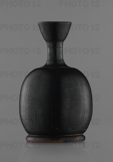 Black-finished aryballoi lekythos, Greek black-glazed pottery. Aryballoi lekythos coated with black varnish. Medium with flat foot flowing directly into a bulging body, significantly widened in its lower section. Nearly horizontal handles flow into a slender neck ending in a markedly widening, cup-shaped rim. Handle attached at the transition from body to handles and below the cup-shaped rim. Body bears an engraved ornament of long, vertically arranged petals. Good condition, minor damage to varnish; neck cracked and glued. 4th century BC, Attic manufacture, vessel lekythos., A dark rounded vase with a narrow neck and flared rim set against a gray background, the vase appears primarily black with subtle brown tones at the rim and base, the body shows vertical carved or molded panels creating a ribbed appearance, the surface has a matte finish with faint lighter scuffs and worn spots, and the base sits on a slightly raised foot that shows more of the brown underlayer.