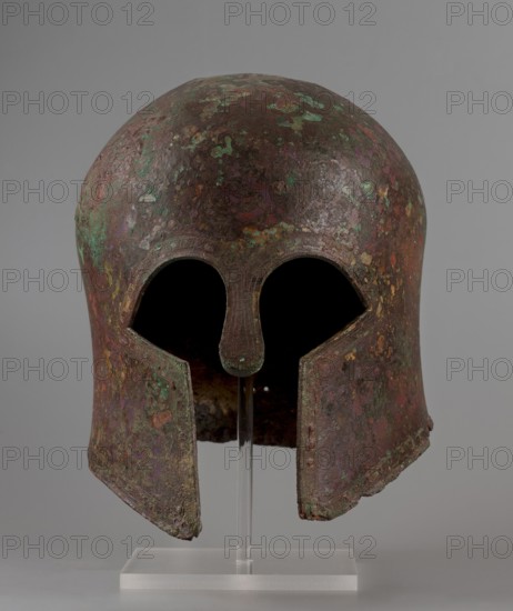 Corinthian-type helmet, This Corinthian-type helmet, with thicker walls in the cheekpieces and a significantly thickened nose plate, has a domed peak, beneath which the walls are slightly concave, widening again at the edge. At the back, near the edge, are two small, round holes for attaching a cord. There is a similar hole in the peak. The edges of the helmet, cheekpieces, and eyeholes are decorated with a precisely crafted band of ornamentation consisting of rectangular fields framed at the top and bottom by a double engraved line and separated by double engraved squares, between which are rows of tiny plastic spheres. A row of similar spheres is located between the lines framing the rectangles at the top. The ornamentation reaches the base of the nose guard, which is decorated only with engraved lines, repeating the shape of the protective plate. Date: 600 BC previously dated 630–600 BC. Place of origin: Sparta Greece, — Mycenae Greece ? according to Otto Schaubert. Function: weapon...