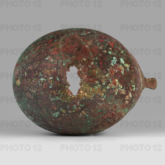 Corinthian-type helmet., Dated ca. 600 BC previously dated 630–600 BC. Possibly from Sparta or Mycenae according to Otto Schaubert. Bronze helmet with thicker cheekpieces and a significantly thickened nose plate; domed peak with slightly concave walls widening at the edge. Two small round holes near the back edge and one in the peak for attaching a cord. Edges of the helmet, cheekpieces, and eyeholes decorated with a precise band of ornament: rectangular fields framed by double engraved lines and separated by double engraved squares, with rows of tiny applied plastic spheres; an additional row of similar spheres between the lines framing the top of the rectangles. Ornamentation reaches the base of the nose guard, which is decorated only with engraved lines repeating the plate’s shape. Function: weapon/helm. Height 23 cm, width 18.2 cm, depth 25 cm, weight 1.322 kg., A roughly spherical object with an irregular hole in its surface sits against a neutral background; the object's surface ...