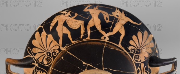Kylix depicting youths at play, Thalia Painter 520–510 BC. A: three naked youths; B: two youths with spears, one with a rhyton. Palmettes at the vices, lotus buds under the vices. At the bottom, a leaning, naked youth. Sport in antiquity iconography. Greek ceramics; Attica; vessel kylix. Weight 1.030 kg. Date: 510–500 BC previous dating c. 520 BC. Thalia Painter fl. 520–510 BC., A shallow curved ceramic vessel fragment with a black background and orange figures and decorative motifs, showing a partial scene of three nude human figures in orange with black detailing positioned along the rim, each in different dynamic poses and one holding a curved object, flanked by large stylized orange palmette motifs with swirling elements on either side; the surface shows visible cracks and areas of wear where the orange slip is chipped, and the vessel has two short black handles extending outward from the lower edges.