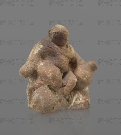 Terracotta figurine of Silenus, Silenus mythology; terracotta. Figurine of an obese Silenus sitting on a rock. The figurine is hollow inside, open at the bottom. The back is only roughly worked, with a large, triangular opening. The clay is red, strongly and unevenly fired; the surface is light, cracked, and mostly chipped. The idol sits frontally, with thighs widely spread and feet crossed. The belly is sagging. The right arm rests with its elbow on the thigh, the forearm and hand stretched slightly downward. The left hand holds a waterskin resting on the rock and the side of the thigh. The small head, slightly lowered, turns to the left and downward, towards the waterskin. Silenus is partially covered by a chlamys, fastened at the right shoulder and thrown back over the left arm; the lower torso and legs are bare. Schematic modeling; head, arms, legs and waterskin rendered synthetically, with a tendency to accentuate volume. Numerous chips and surface flaking. Wide crack in the base ...