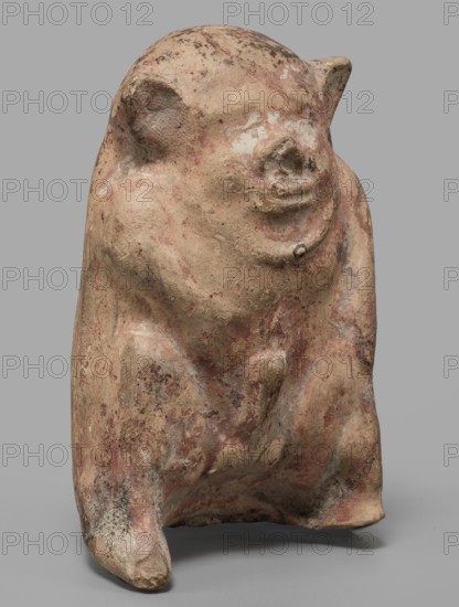 Figurine of a crouching satyr, Greek deities, Satyr myth., mold-impressed terracotta figurine, 6th–5th century BC formerly dated to beginning of 5th century BC, Rhodes; height 7.5 cm, width 4.8 cm, depth 3.8 cm, weight 0.05 kg, A weathered sculptural form resembling a seated animal figure with a rounded head and small rounded ears, rendered in an earthy beige tone with visible patches and streaks of muted red and darker brown; the surface shows rough texture and worn areas with some lighter off-white spots and darker smudges, and the figure rests on a flat gray surface against a neutral gray background.
