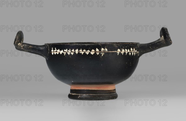 Kylix gnathia, scene: gal/class, southern Italian pottery, plant motifs, end of 4th–beginning of 3rd century BC previously dated 3rd–2nd century BC, Southern Italy Italy; vessel kylix; height 6.3 cm, width 13.9 cm, depth 8.4 cm, weight 0.088 kg., A shallow bowl-shaped vessel with a rounded body and a low pedestal base, shown from the front with two horizontal handles extending outward and curving upward at each side; the vessel is predominantly black with a band of small light-colored leaf-like shapes encircling the upper exterior, and a thin light line beneath that band; the base area shows a narrow reddish-brown band above the foot which is also black; the surface has worn areas and small spots where the black coating is chipped, revealing lighter material beneath; the background is a smooth grey.