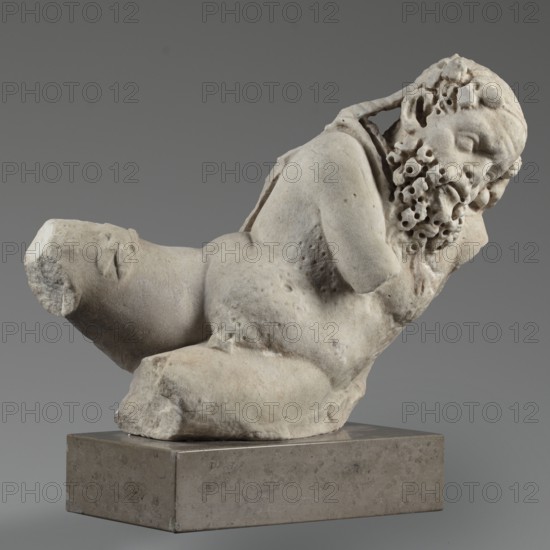 Reclining Silenus, unknown Roman workshop, Scen.Gal.Class., architectural elements, Silenus mythology, Roman sculpture, Sculpture of a reclining Silenus supported on his left hip and elbow, 69–79, Roman Empire 27 BC–476, sculpture; height 29.4 cm, width 37 cm, depth 22 cm, weight 19.4 kg, A weathered light-gray stone sculpture of a reclining bearded male figure rests on a darker gray rectangular base; the figure shows a turned head with a textured, curly beard and closed eyes, a rounded torso with subtle pitting and surface irregularities, an arm bent near the head, and broken or truncated limbs, all set against a smooth medium-gray background with soft lighting.