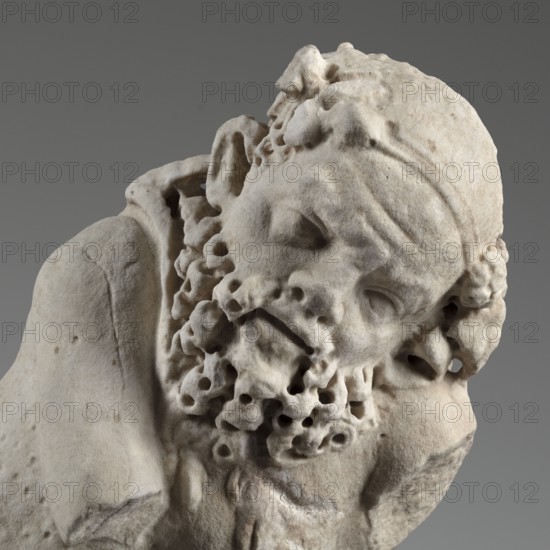Reclining Silenus, unknown Roman workshop, architectural elements, Silenus mythology, Roman sculpture — Sculpture of a reclining Silenus supported on his left hip and elbow, dated 69–79 CE, Roman Empire 27 BC–476, sculpture; height 29.4 cm, width 37 cm, depth 22 cm, weight 19.4 kg, A close-up of a pale beige stone sculpture of a bearded head and upper torso set against a neutral gray background, showing textured, weathered surfaces and carved curls in the beard and hair, with deep-set eye sockets, a furrowed brow, and a tilted head resting slightly to one side, the stone displaying subtle variations of off-white, cream, light gray, and faint brownish tones.