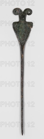 Pin, unknown Luristan workshop. Pin with a thin, oval shaft transitioning into a flat head composed of an upside-down triangle base, from the center of which grows a rectangle that bisects into two small volutes. 8th–6th century BC; Iron Age II 1st half of 1st millennium BC. Luristan, Iran. Ornament. Height 18.1 cm; width 3.1 cm. Materials: bronze Luristan bronzes. Makers/attribution: unknown., An elongated metal object with a long slender pointed shaft topped by a wider flattened section that narrows into a decorative head; the head has a triangular shield-like body and two symmetrical curled spiral terminals. The surface shows irregular texture and wear with mottled tones of dark brown, dark green, and hints of black and verdigris. The background is a plain light gray.