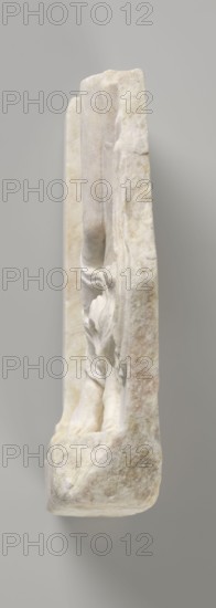 Fragment of a relief with a dancing maenad, 1st century BC, 27 BC–14 period of the rule of Octavian Augustus, Roman Empire, bas-relief, height 35 cm, width 30 cm, thickness 6.5 cm, A narrow vertical view of a carved stone slab shown from the side, displaying a pale off-white and beige surface with areas of light gray and subtle warm tan mottling, the stone's edge is rough and irregular while the carved relief visible along the inner face shows smooth undulating folds and rounded forms, the background is a uniform soft gray.