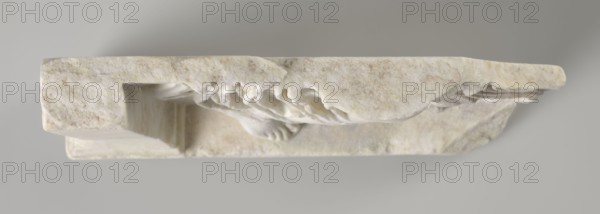 Fragment of a relief with a dancing maenad, 1st century BC, 27 BC–14 AD period of the rule of Octavian Augustus, early Roman Empire, bas-relief, height 35 cm, width 30 cm, thickness 6.5 cm, A horizontal stone relief piece photographed against a neutral gray background, showing a carved surface with a rough, weathered texture and a pale off-white color with beige and light brown mottling; the relief includes a recessed rectangular cavity and a sculpted draped form with flowing folds and rounded contours in a slightly brighter white, and the stone edges display irregular chips and varied thicknesses with subtle shadowing.