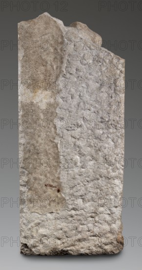 Fragment of a sarcophagus depicting the daughter of King Lycomedes, unknown Roman workshop, Classified Gallic Scenography, Lycomedes mythology, Roman art, late 2nd–3rd century, Roman Empire 27 BC–476, bas-relief, sarcophagus Roman, height 77 cm, width 32.5 cm, depth 16 cm, weight 63.5 kg, A tall, roughly rectangular stone slab with an uneven, broken top and a rough, textured surface; the slab shows a split of surface tones with one side appearing light gray and the other side a brownish-beige, along with areas of darker brown and subtle yellowish discoloration; the stone has pitted, irregular contours and visible chipping along edges and base, and the background is a smooth gradient of dark gray.