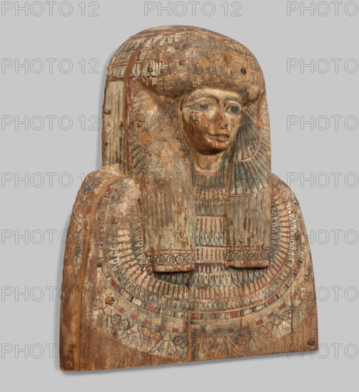 Fragment of a sarcophagus lid. Part of the lid of an anthropoid woman's sarcophagus. Large, striped wig falling on the breasts at the front, decorated with four diadems of lotus petals and vulture wings, and bands of rosettes at the ends. On the breast is a multi-row necklace, with lotus flowers and rosettes forming the lower row. Lotuses, vulture vulture wings, element of the so-called vulture diadem, necklace, wigs, funerary equipment, lotus flower decorative motif. Egyptian art. c. 945–c. 735 BC; Third Intermediate Period, 22nd Dynasty, Egypt. Sarcophagus. Height 62 cm; width 49 cm; depth 20 cm., A carved wooden funerary panel shaped like a bust with a stylized head and shoulders, showing worn painted surface and areas of flaking and loss; the face has carved eyes, nose, and mouth with traces of darker pigment around the eyes and mouth, and the hair or headdress is rendered as a rounded, layered wig that extends down over the shoulders. The chest area is decorated with a wide, ornat...