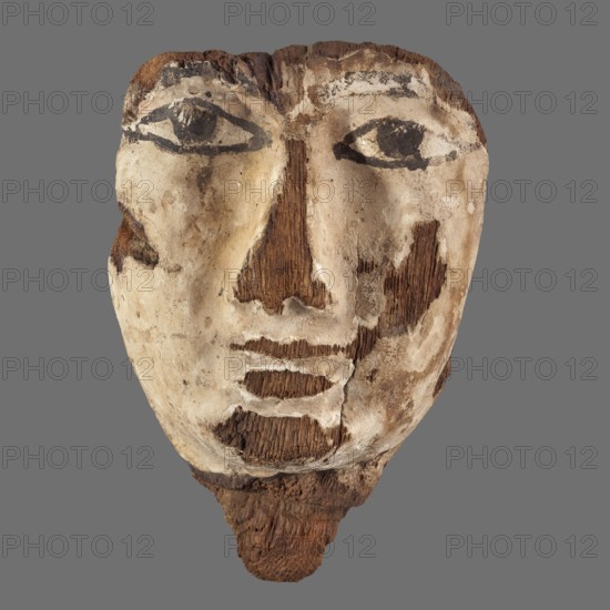 Sarcophagus mask with a small neck fragment, painted cream. Eyes highlighted with black paint. 332–30 BC; Ptolemaic Period, Egypt. Sarcophagus mask., A weathered mask-like face made of rough wood and worn pale plaster fills the frame against a gray background, showing a group of textured brown wooden areas where the material has exposed grain, surrounded by creamy off-white and beige plaster patches; dark black paint forms the outlines of large almond-shaped eyes and thicker dark brown to black markings accentuate parts of the brows and mouth, while various brown stains and scuffs create mottled darker areas on the cheeks and chin, and the lower edge tapers into a jagged darker brown wooden projection.