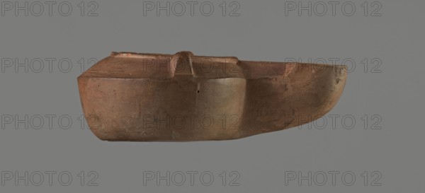 Lamp with a tragic mask, unknown Italian workshop. Oil lamp, single-burner, Roman, Buchi type IX-b = Loeschcke type IXb. Lamp from a mold. Round vessel with arms drooping to the outer, separated from the disc by a convex edge. Two bars arranged symmetrically on the arms. Concave, flat disc with two olive holes located on either side of the convex representation in the form of a theatrical tragic mask. Medium-length wick channel, decorated with a groove in the center and a small air ventilation hole in the center of the groove. Rounded end of the burner. Slight trace of use dark discoloration near the wick hole. On the bottom, a convex inscription workshop trademark: COMMUNIS. Compare with MNW 236765, second half of the 1st/beginning of the 2nd century, Modena. Dimensions: height 9 cm, width 4.4 cm, depth 3.3 cm., A brownish clay object with a smooth, rounded body and a flattened top, showing a few subtle surface imperfections and small pits, set against a neutral gray background; the o...