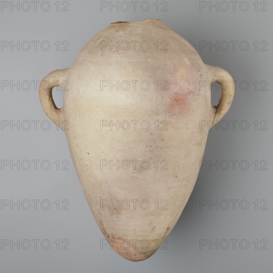 Large ovoid amphora with rounded foot, clay MD marl, Vienna System. Body wheel-made; hand-made foot. Two small vertical handles placed at greatest bulge at base of the sloping arms; sloping arms symmetrically placed with two black-painted inscriptions labels/dockets on their bases. Above one handle, slightly toward the center, are impressed cartouches of Hatshepsut and Thutmose III and a snake hieroglyph dz. Potter’s mark of two intersecting lines beneath one handle. Surface even; color very light brown. Incomplete—neck and spout missing. New Kingdom, 18th Dynasty reign of Hatshepsut and Thutmose III, ca. 1550–1295 BC. Preserved height 49.5 cm; diameter at belly 30.5 cm., A large, rounded clay vessel with a tapered pointed base and a narrow top, shown against a gray background; the vessel has a matte, textured surface in pale beige and tan tones with areas of light pink and faint reddish patches, and it features a pair of looped handles on opposite sides that are similar in color and t...