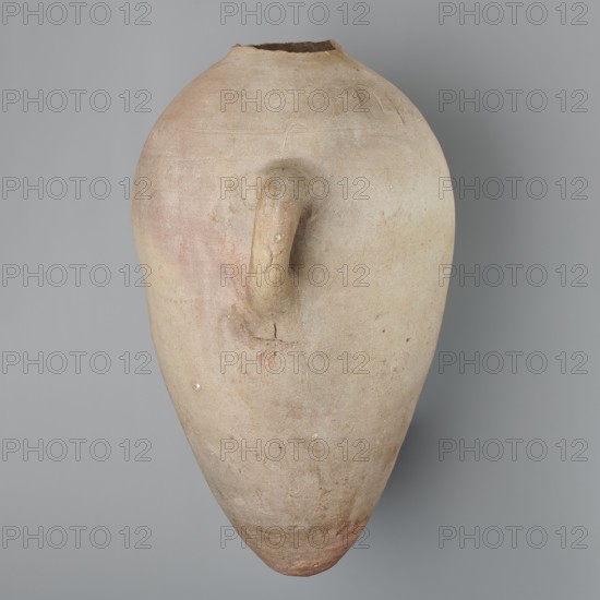 Large ovoid amphora with rounded foot, clay MD-type marl, Vienna System; body wheel-made, foot hand-made; surface even; color very light brown; neck and spout missing. Two small vertical vices on the body at the greatest bulge at the base of the handles; sloping handles symmetrically placed with two black-painted inscriptions labels/dockets on their bases. Above one vice, slightly toward center, are impressed cartouches of Hatshepsut and Thutmose III and a snake hieroglyph dz. Under one vice is a potter’s mark of two intersecting lines. New Kingdom, 18th Dynasty reign of Hatshepsut and Thutmose III, ca. 1550–1295 BC; height preserved 49.5 cm, belly diameter 30.5 cm., An elongated clay vessel with a rounded top and a tapered, pointed bottom, showing a roughly textured surface in muted beige and tan with areas of pale pink and light brown; a curved handle projects from the upper body, blending into the vessel’s surface where there are small chips and a visible crack, and the rim at the t...