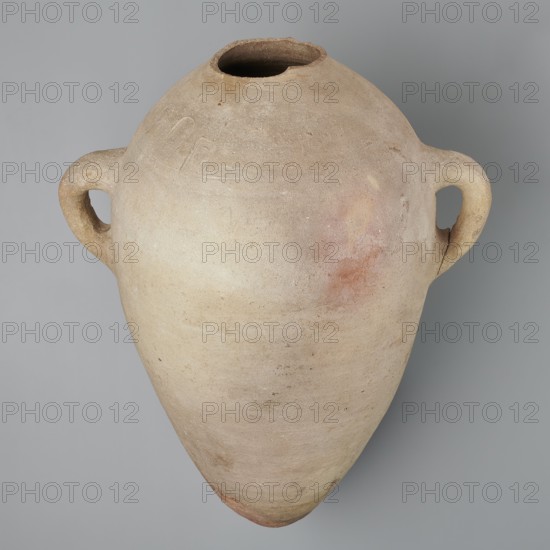 Large amphora with an ovoid shape and a rounded foot. Two small vertical vices placed on the body at the point of its greatest bulge at the base of the arms. The foot is hand-made; the body was wheel-made. Made of MD type marl clay Vienna System. Surface even. Sloping arms, with inscriptions in black paint labels, dockets symmetrically placed on both sides of the body. Above one of the vices, slightly toward the center of the body, are impressed cartouches of Hatshepsut and Thutmose III and a snake hieroglyph dz. Under one of the vices, a potter's mark of two intersecting lines. Very light brown color. Incomplete — neck and spout missing. New Kingdom, 18th Dynasty reign of Hatshepsut and Thutmose III, ca. 1550–1295 BC. Two cartouches of Hatshepsut and Thutmose III; two labels on the body. Preserved height 49.5 cm; belly diameter 30.5 cm., A large, rounded clay vessel with a tapering pointed base and a wide, irregular mouth, shown against a flat neutral background. The vessel has a pair...