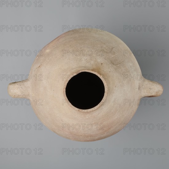 Large amphora with an ovoid shape and a rounded foot. Two small vertical vices placed on the body at the point of its greatest bulge at the base of the arms. The foot is hand-made, the body wheel-made. Made of MD type marl clay Vienna System. Surface even. Sloping arms, along their bases on both sides of the body, are symmetrically placed with inscriptions in black paint labels, dockets. Above one of the vices, slightly toward the center of the body, are impressed cartouches of Hatshepsut and Thutmose III and a snake hieroglyph dz. Under one of the vices, a potter's mark of two intersecting lines. Color very light brown. Vessel incomplete — neck and spout missing. Cartouches of Hatshepsut and Thutmose III; two labels on the body. New Kingdom, 18th Dynasty reign of Hatshepsut and Thutmose III, ca. 1550–1295 BC; findspot: Deir el-Medina grave 1370 f. Preserved height 49.5 cm; belly diameter 30.5 cm., A top-down view of a rounded vessel with a wide central opening and a few small protrudi...