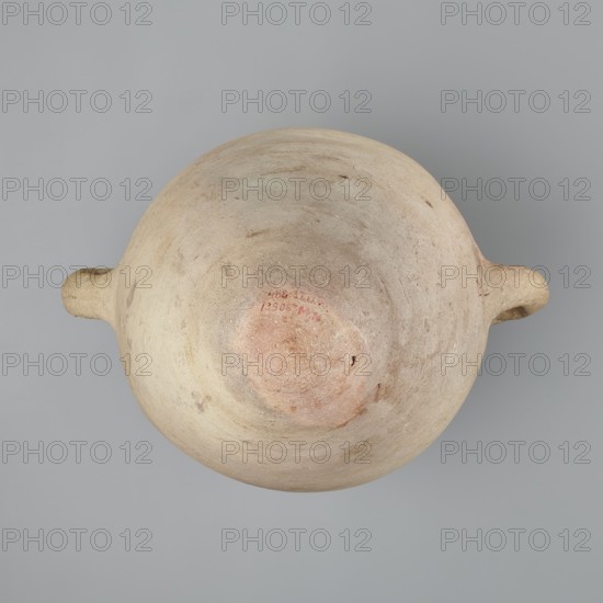 Large amphora with an ovoid shape and a rounded foot. Two small vertical vices placed on the body at the point of its greatest bulge at the base of the arms. The foot is hand-made; the body was wheel-made. Made of MD type marl clay Vienna System classification. Surface even. Sloping arms symmetrically placed with inscriptions in black paint labels, dockets. Above one vise, slightly toward the center, are impressed cartouches of Hatshepsut and Thutmose III and a snake hieroglyph dz. Under one vise, a potter's mark of two intersecting lines. Color very light brown. Vessel incomplete—neck and spout missing. Cartouches of Hatshepsut and Thutmose III; two labels on the body. New Kingdom, 18th Dynasty reign of Hatshepsut and Thutmose III, ca. 1550–1295 BC. Findspot: Deir el-Medina grave 1370 f. Preserved height 49.5 cm; belly diameter 30.5 cm., A top-down view of a round, weathered ceramic vessel with a domed center and two small horizontal handles on opposite sides, showing a textured surfa...