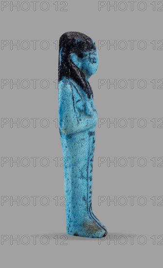 Queen Maatkare's shabti, Divine Wife of Amun, cartouches, hieroglyphs, uraeus iconographic, Maatkare ca. 1069–945 BC, wigs, funerary figurines, grave goods, mummy-shaped figurine. Arms crossed on the chest, the right folded over the left. Hoes in each hand. On the back is a basket slung on strings over both shoulders. Facial details, wig, and tools painted in a dark color. On the head is a three-part smooth wig with a uraeus above the forehead. Bracelets on the wrists. Painted inscription on the front of the legs in one wide column framed with lines: Shd Osiris, the wife of the god, the lord of both lands, Maat-ka-re. Owner: Osiris, the divine wife of the lord of both lands, Maatkare; ca. 1069–ca. 945 BC; Third Intermediate Period; 21st Dynasty, Egypt. Shabti; height 12 cm, width 4.4 cm., A small standing figurine shown in profile with a smooth elongated body and a rounded head, displaying a few raised arms folded across the chest and a long hairstyle that falls along the back; the sur...