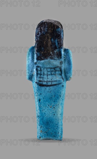 Queen Maatkare's shabti, Divine Wife of Amun, cartouches, hieroglyphs, uraeus iconographic, Maatkare ca. 1069–945 BC, wigs, funerary figurine, grave goods, mummy-shaped figurine. Arms crossed on the chest, right folded over left, hoes in each hand. On the back is a basket slung on strings over both shoulders. Facial details, wig, and tools painted in a dark color. Three-part smooth wig with a uraeus above the forehead. Bracelets on the wrists. Painted inscription on the front of the legs in one wide column framed with lines reading: Shd Osiris, the wife of the god, the lord of both lands, Maat-ka-re. Third Intermediate Period, 21st Dynasty, Egypt. Shabti, height 12 cm, width 4.4 cm., A small elongated figurine shown against a solid gray background with a rounded top and a tapering lower section, predominantly bright turquoise blue with speckled darker blue and tiny brownish spots, a darker almost black area covering the rounded top and upper back, a pair of short stubby projections at ...