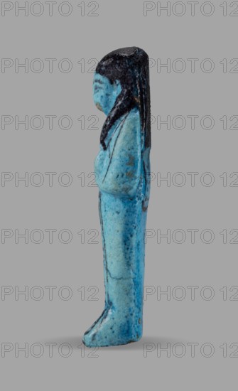 Queen Maatkare's shabti, Divine Wife of Amun, cartouches, hieroglyphs, uraeus iconographic, Maatkare ca. 1069–945 BC, wigs, funerary figurine, grave good, mummy-shaped figurine. Arms crossed on the chest, the right folded over the left, holding hoes in each hand. On the back is a basket, slung on strings over both shoulders. Facial details, wig, and tools painted in a dark color. Three-part smooth wig with a uraeus above the forehead; bracelets on the wrists. Painted inscription on the front of the legs in one wide column framed with lines: Shd Osiris, the wife of the god, the lord of both lands, Maat-ka-re. Third Intermediate Period; 21st Dynasty, Egypt. Shabti; height 12 cm, width 4.4 cm., A small upright figurine shown in profile with a smooth blue body and darker blue to black hair that falls down the back; the figure's arms appear folded across the chest and the surface shows mottled blue tones with a few darker speckles and slight worn areas; the background is a uniform light gra...