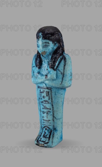 Queen Maatkare's shabti, Divine Wife of Amun, cartouches, hieroglyphs, uraeus iconographic, Maatkare ca. 1069–945 BC, wigs, funerary figurines, grave goods, mummy-shaped figurine. Arms crossed on the chest, the right folded over the left. Hoes in each hand. On the back is a basket slung on strings over both shoulders. Facial details, wig, and tools painted in a dark color. On the head is a three-part smooth wig with a uraeus above the forehead. Bracelets on the wrists. Painted inscription on the front of the legs in one wide column framed with lines: Shd Osiris, the wife of the god, the lord of both lands, Maat-ka-re. Owner: Osiris, the divine wife of the lord of both lands, Maatkare; ca. 1069–945 BC; Third Intermediate Period, 21st Dynasty, Egypt. Shabti; height 12 cm, width 4.4 cm., A small statuette of a standing human figure in shades of blue with darker blue to black hair and facial detailing, arms crossed over the chest, a long garment extending to the feet with darker linear mar...