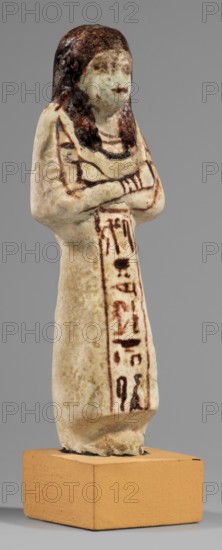 Ushabti of Mrs. As, hieroglyphs, As ca. 1295–1069 BC, Minutoli, Alexander von 1806–1887, usekh necklace, hoes, wigs, grave goods, figurine in living costume, loincloth reaching to the ankles. Arms crossed on the chest, right folded over left. Hoes in both hands, basket on the back slung over both shoulders. A usekh necklace on the chest, wide bracelets on the wrists. On the head is a smooth, double wig. Round face, poorly defined nose, narrow mouth, large eyes. The wig, eyes, eyebrows, mouth, necklace, bracelets, hoes, and bag are painted in brown with a burgundy tint. The inscription is painted. The inscription runs in one vertical line on the front of the headband. Text: Shd Osiris, Lady of the House of As. c. 1295–c. 1069 BC; New Kingdom, 19th–20th Dynasty, Egypt, shabti; height 13.2 cm, width 4.5 cm, A small standing figurine with a rounded head and folded arms, mounted on a rectangular block. The figure has dark brown hair painted over the head and upper shoulders, a pale off-whit...