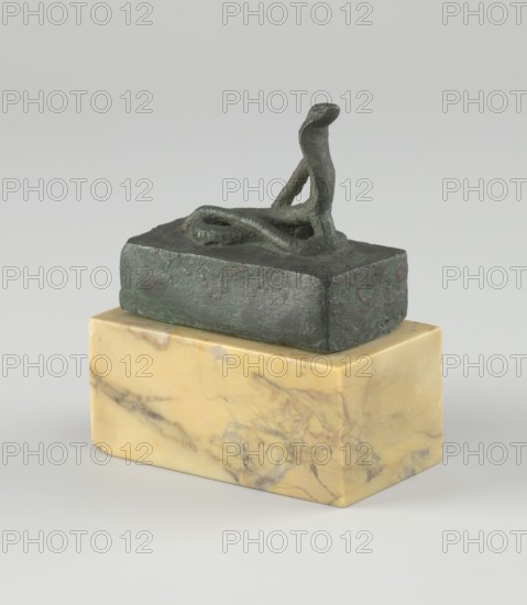 Snake sarcophagus, snakes, Atum mythology, Renenutet mythology, reliquaries, sacred animals. Snake with raised head, coils on a rectangular reliquary-sarcophagus—probably the cobra Renenutet, although it may also be Atum. 664–332 BC; Late Period, Egypt. Figurine; height 3.3 cm, width 5.5 cm, depth 5 cm., A small bronze sculpture with a rough textured dark green and brown patina sits on a rectangular polished stone base that is yellow with beige and brown veining; the bronze piece features a simplified looping form rising into an elongated curved element, and the background is a smooth light gray.