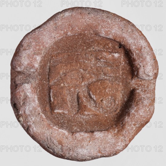 Amulet mold - udjat eye, udjat eye iconography, amulets, castings, 664–332 BC; Late Period, Egypt, mold, height 1.5 cm, width 3.9 cm, depth 3.8 cm, A round, flattened object with an uneven rim and a recessed central area, showing a coarse, grainy texture. The surface appears mostly reddish-brown with patches of lighter, pale beige or off-white dusting. The recessed center contains shallow, roughly geometric impressions and worn irregularities, and the rim shows chips and small pits. Overall the colors visible are reddish-brown and pale beige, with subtle variations in tone across the surface.