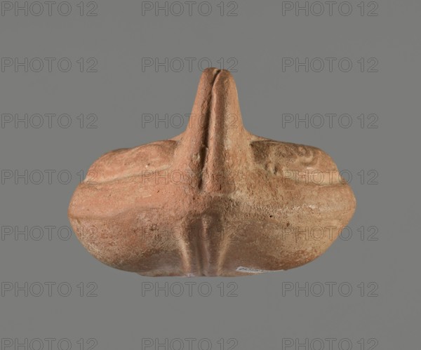 Oil lamp, Horse iconography. Lamp pressed from a mold. Light red clay with brownish-red engobe. Almond-shaped container. Ring-shaped, slightly concave base with a mold mark of two notches letter lambda or simplified alpha. A single groove runs from the base towards the vise. Solid vise. Arms decorated with a simplified winding vine s-scroll motif. Slightly concave disc with two olive holes, decorated with a depiction of a horse galloping left. Medium-length burner with an oval end and a round wick hole. No traces of use. 4th–5th century, Tunisia place of origin. Oil lamp; height 10.7 cm, width 6.9 cm., A roughly symmetrical, rounded object with a central raised ridge and a vertical protrusion, shown against a flat gray background. The surface appears textured and worn, with a coarse, sandy look. Visible colors include terracotta, muted brown, pale beige, and hints of dusty orange, with lighter worn areas and slightly darker recessed lines. The shape suggests layered contours and soft c...