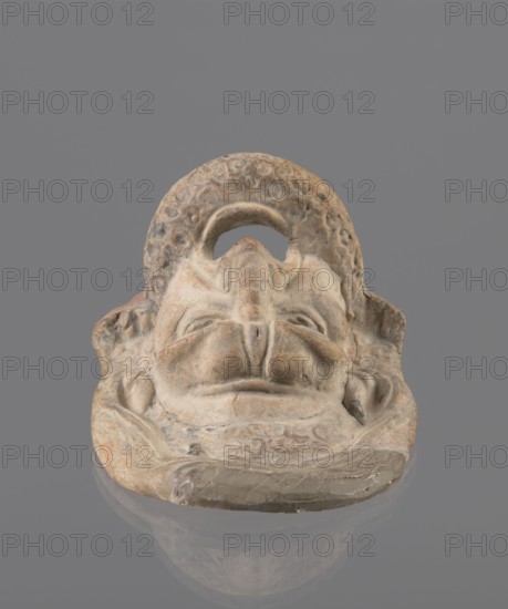 Tragic mask, terracotta, 4th/3rd century BC, Southern Italy. Tragic mask depicting a male face, likely a decorative element antefix?. The lower part, with the beard its underside edges are flat, is set at a near-perpendicular angle to the facial part and forms the base. Realistic theatrical features: protruding cheekbones, deep furrows around mouth and eyes, wide-open mouth with almost horizontal lower lip and arched upper lip. Large, deep-set eyeballs with circular cut-out holes at slightly different heights right higher than left. Slightly hooked nose with horizontal wrinkles, thick eyebrows, vertical forehead wrinkles, and a convex forehead. Above the forehead is a flat, high onkos with schematically marked locks of hair, bounded by folds of cloth. Light orange clay, unevenly fired at the fracture turning red. Traces of polychrome—red paint on the cheek, black on the beard and hair. The upper right part above the forehead has been reconstructed., A sculpted stone or clay mask restin...